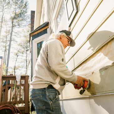 Man using a power sander on house siding outdoors.