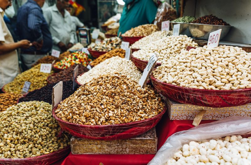 Variety of nuts, raisins, and snacks on display in vibrant baskets within a bustling market.