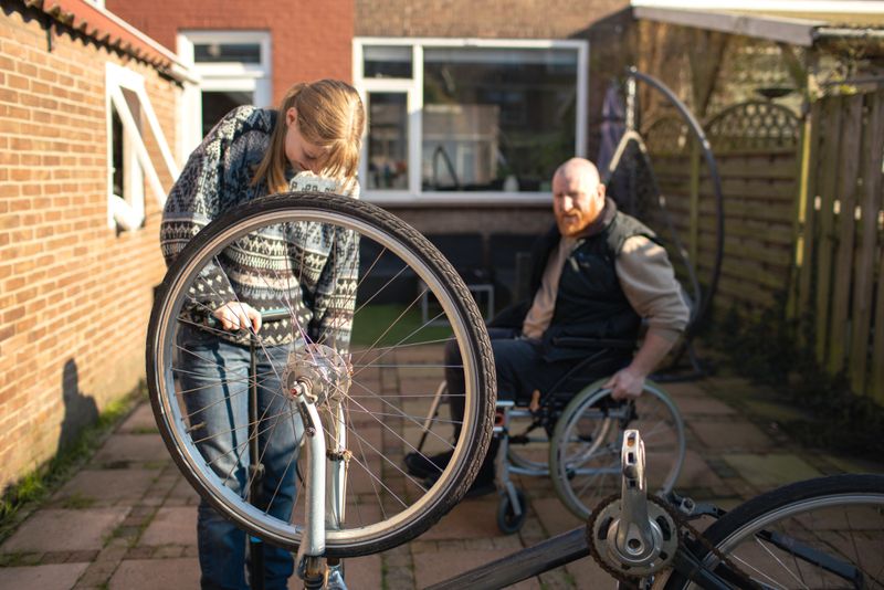 A disabled redhead father and his beautiful blonde daughter fixing a bike together in the garden on a sunny winter's day