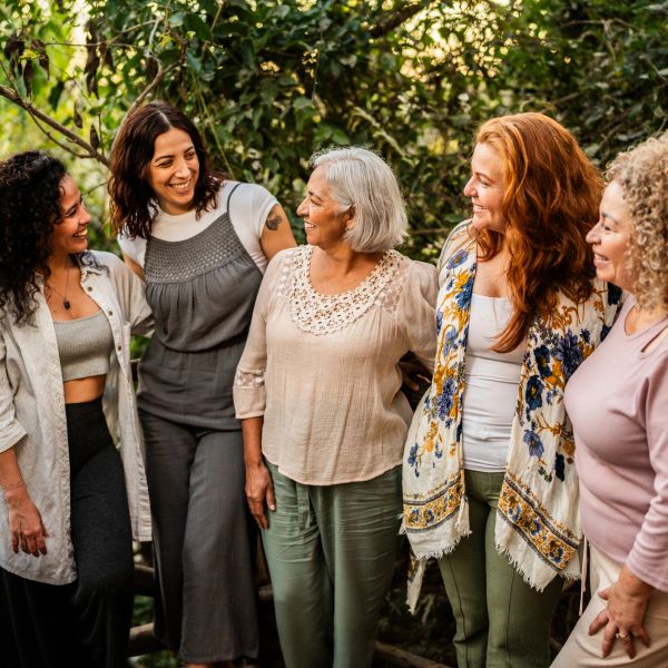 Five women happily chatting outdoors in a green forest setting.