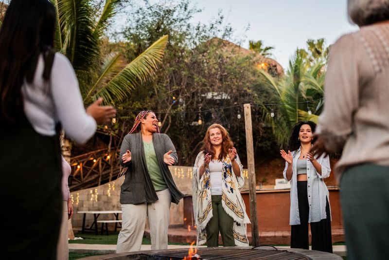 Women singing and applauding around the bonfire outdoors