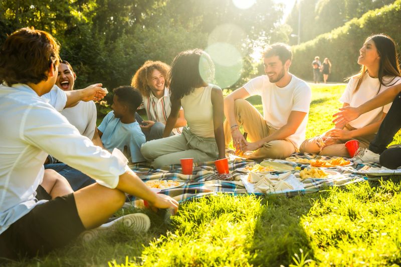 Cheerful friends sharing food and laughter during a vibrant outdoor picnic in a sun-drenched park