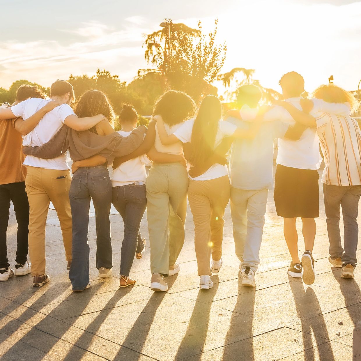 Group of friends walking arm in arm at sunset outdoors.