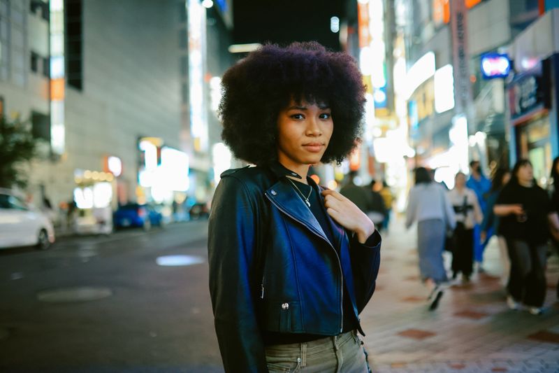 Fashionable young woman with Afro hair on the streets of Tokyo, Japan. She is wearing a stylish leather jacket, lit by the neon lights.