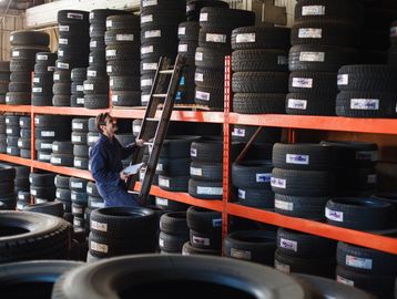Man checking inventory of stacked tires in a warehouse.