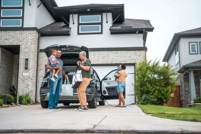 Family unloading bags from car in front of modern house.