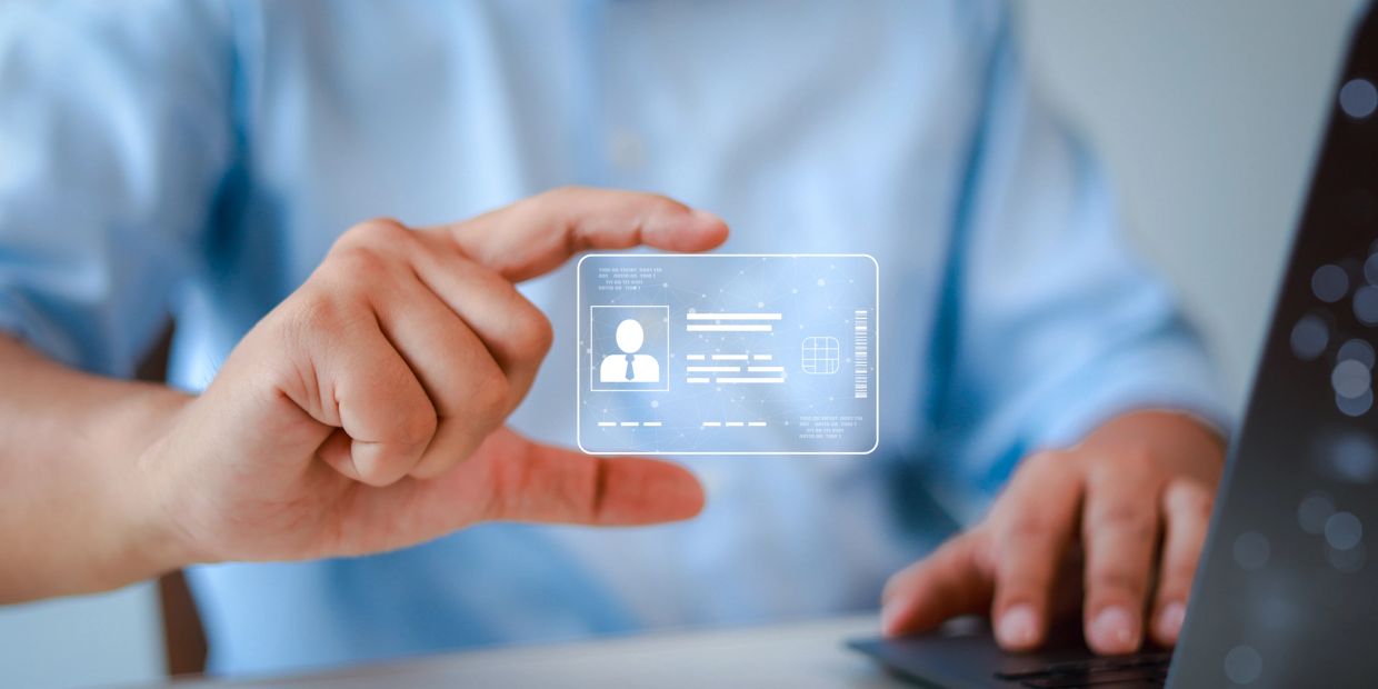 Hand holding a digital ID card hologram near a laptop.