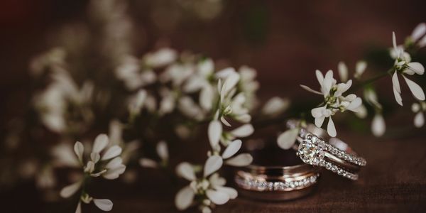 Two sparkling wedding rings amidst delicate white flowers on a wooden surface.