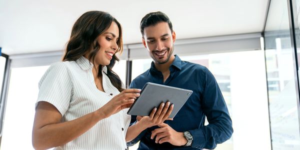 Two professionals smiling and looking at a tablet in a modern office.