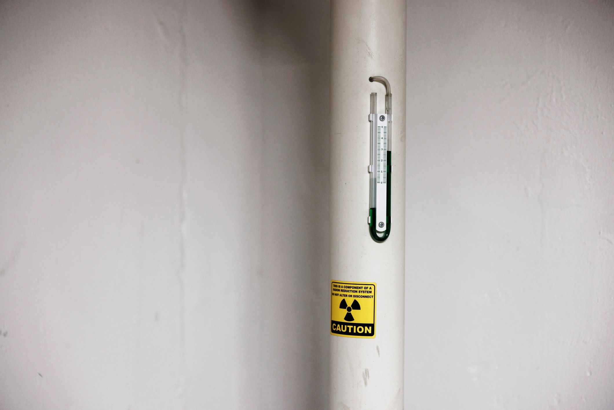 A radon reduction system pipe with a caution label and a gauge.