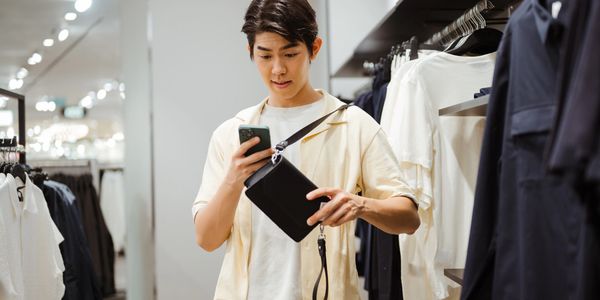 Young man shopping for clothes while checking his phone in a store.