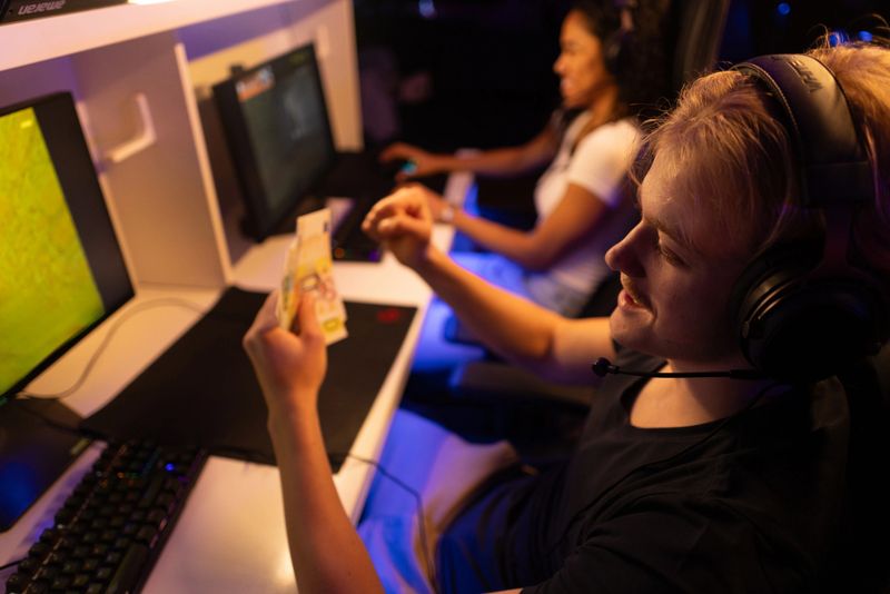Young man holding money while  playing eSports with his girlfriend on PC in gaming club