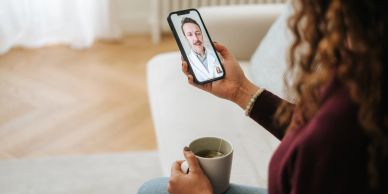 Person video calling a counselor while holding a cup of tea.