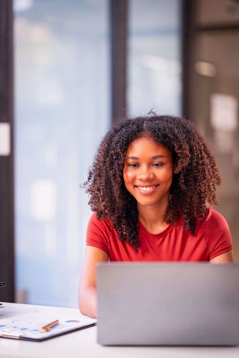 African female employee working night in office with bokeh lights to work late on project deadline using smartphone technology and laptop, graph document
