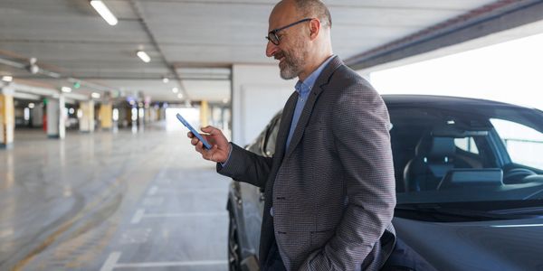 Man leaning on car in parking garage, looking at phone.