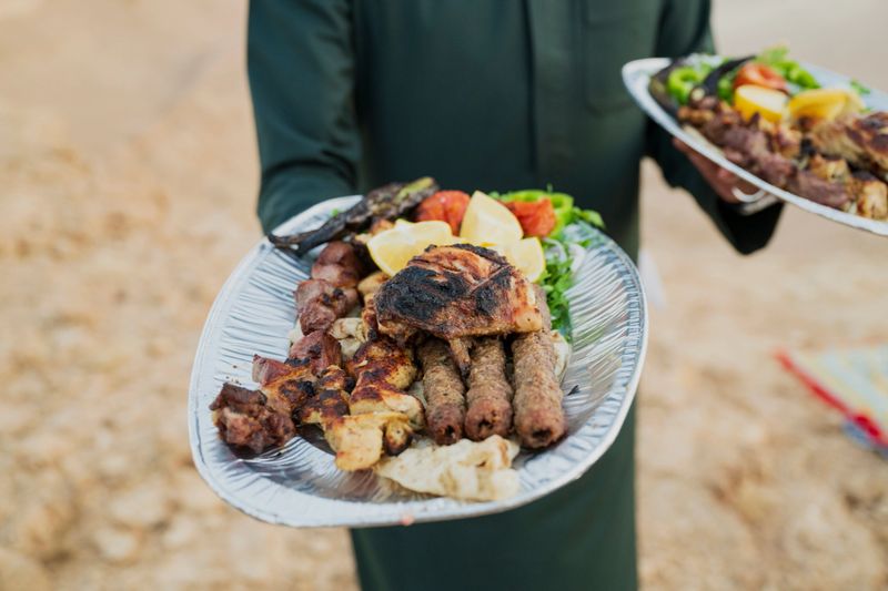 Saudi man in thawb standing outdoors holding cooked meat and vegetables at Edge of the World.