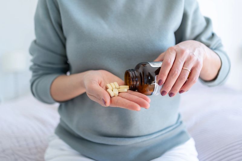 Woman Taking Handful Pills From Bottle In Bedroom