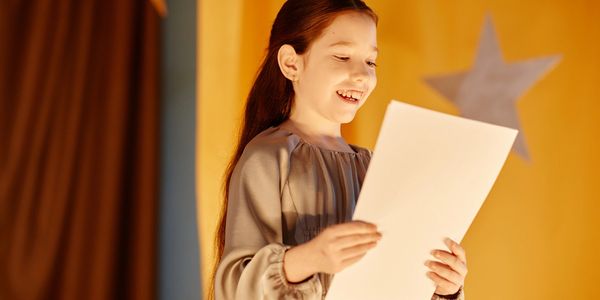 A girl happily reading a paper on stage.