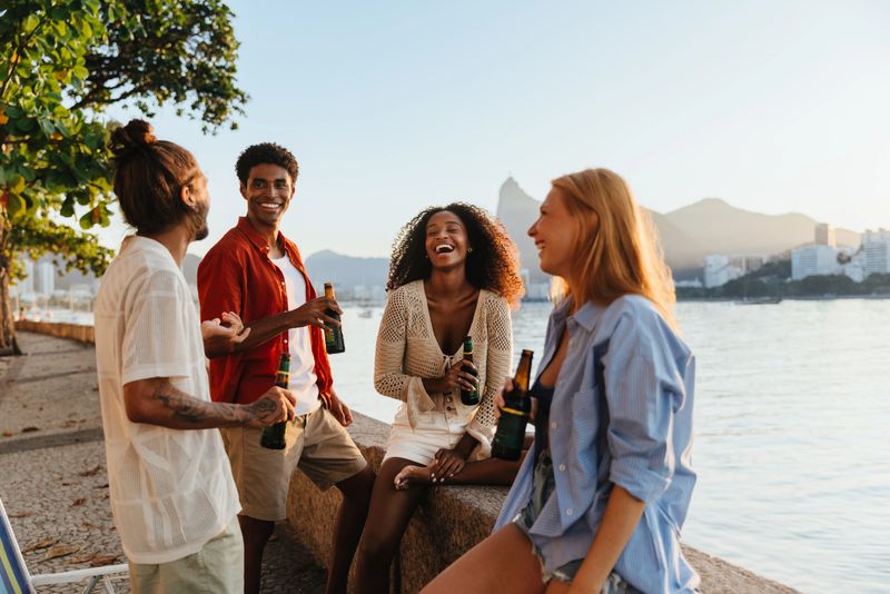 A group of diverse friends enjoying drinks together at the scenic Mureta Da Urca. The backdrop features Corcovado Hill, creating a joyful and vibrant atmosphere.