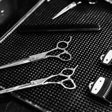 Close-up of barber tools including scissors, combs, and clipper guards on a textured mat.