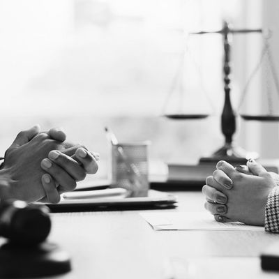 Two professionals in a legal consultation with folded hands and scales of justice.