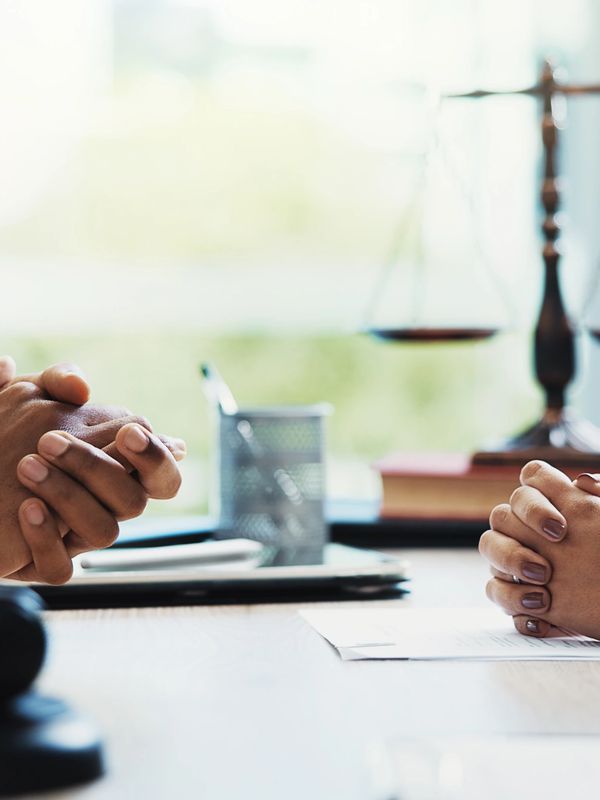 Two professionals in a legal consultation with folded hands and scales of justice.