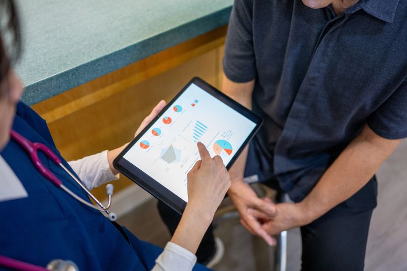 Close up shot of an Asian female doctor discussing a patient's healthcare data report on a digital tablet with an Asian male patient in a hospital.