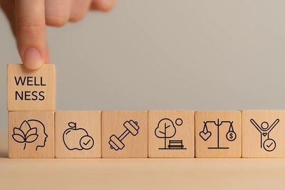 Wooden blocks with wellness symbols and a finger placing the word 'WELLNESS'.