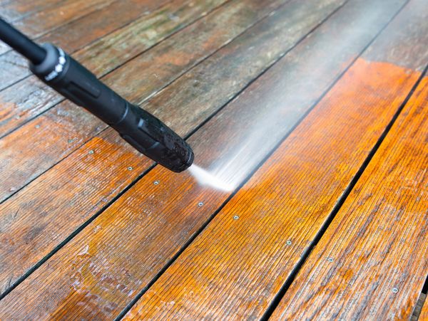 Pressure washing a wooden deck to remove dirt and grime.