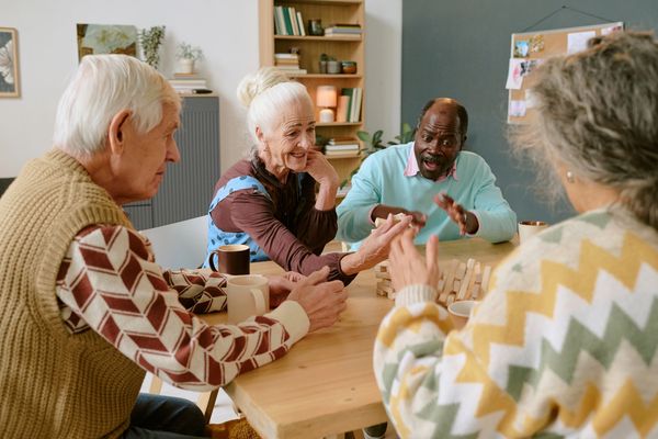 Seniors joyfully playing a game of Jenga together at a wooden table.