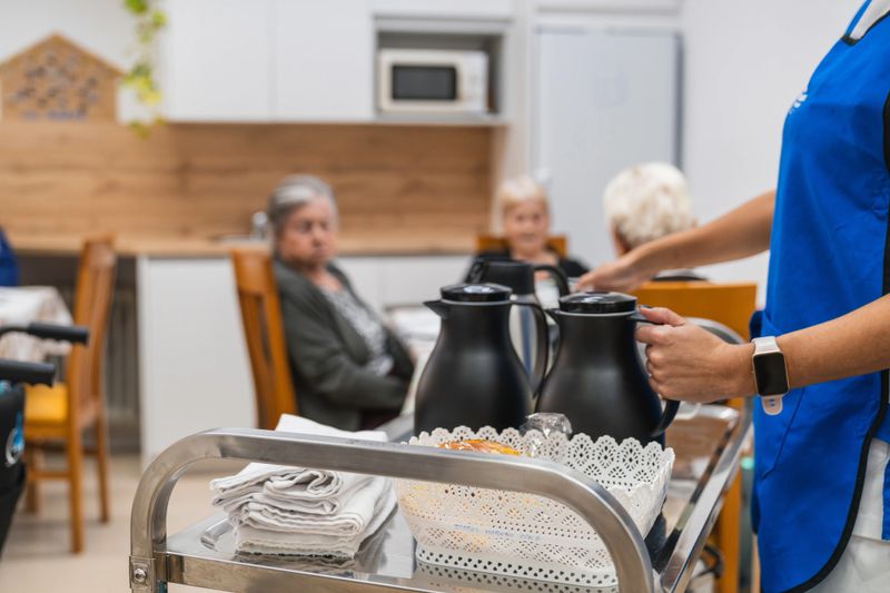 Caregiver serving beverages to senior adults in a modern nursing home kitchen, emphasizing care and attention to residents