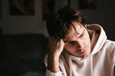A man in a hoodie looks thoughtfully to the side in a dimly lit room.