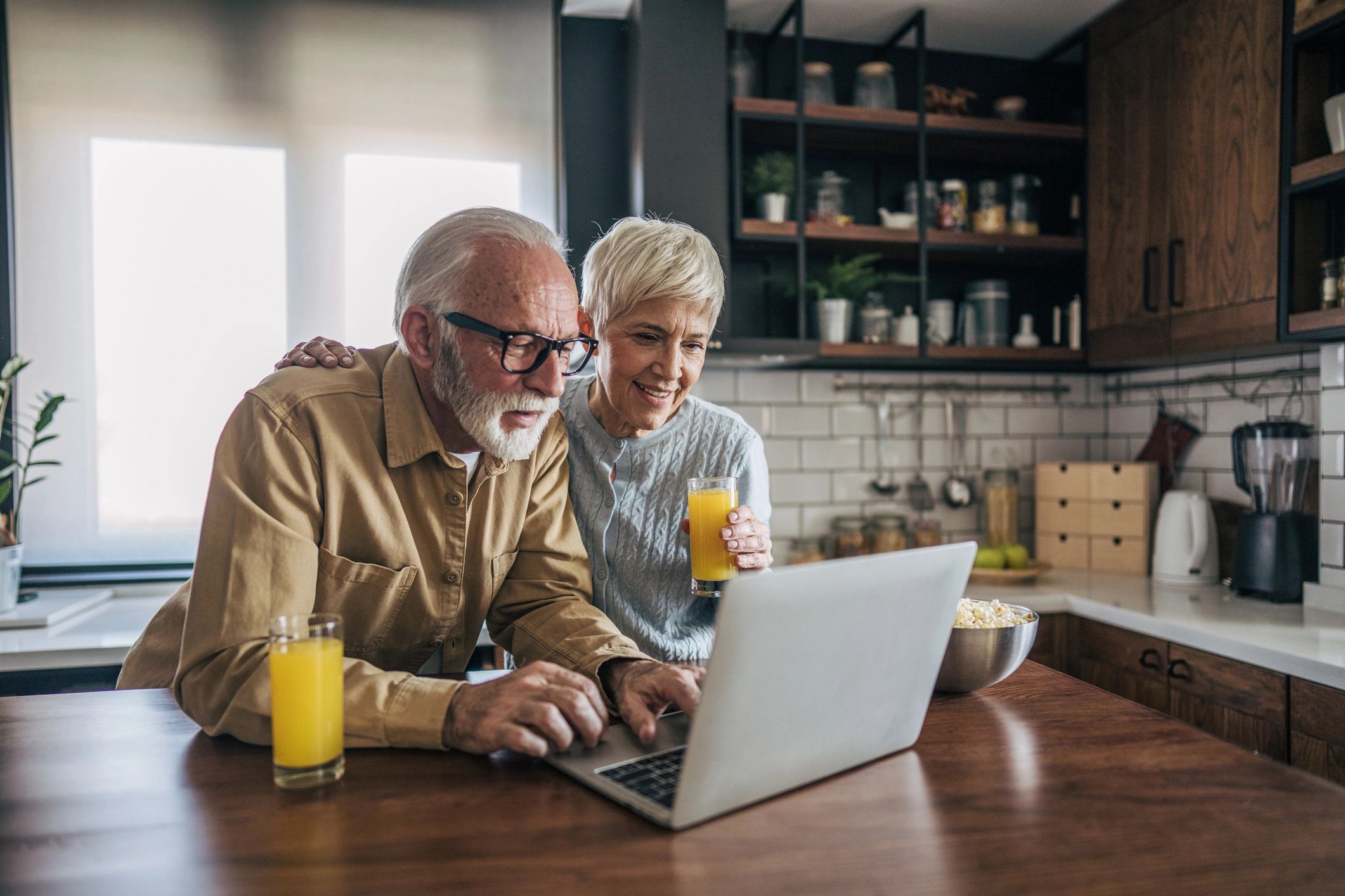 Elderly couple using a laptop in the kitchen.
