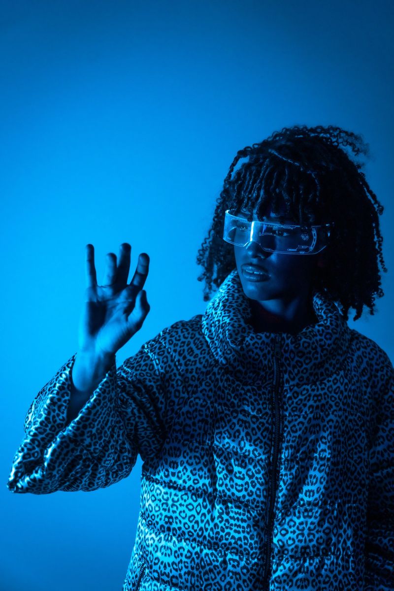 Young black woman wearing futuristic glasses interacts with a hologram, illuminated by blue light