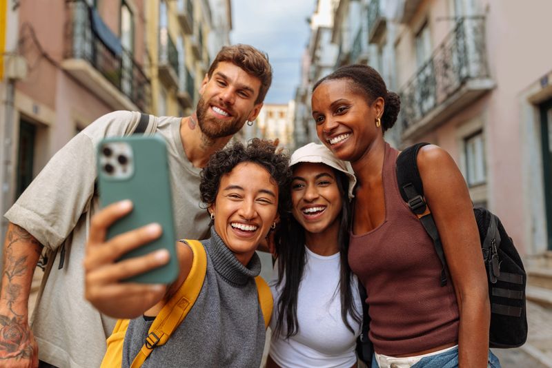 Group of four young adults smiling and taking a selfie while enjoying the vibrant atmosphere of a city street
