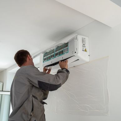 Technician installing a wall-mounted air conditioner indoors.