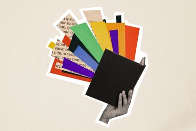 Hand holding a black book with colorful paper and text cutouts bursting out.