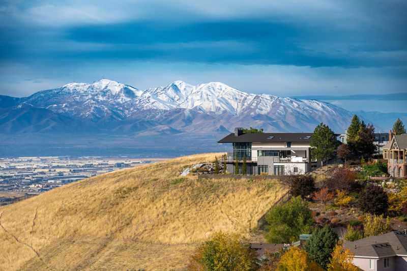 Breathtaking hillside living in Salt Lake City Utah, featuring modern luxury homes overlooking golden fields and snow-capped mountains. This scenic view captures the beauty of nature blending with contemporary architecture in a stunning elevated setting.