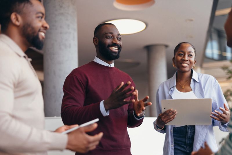 Smiling african businessman leading a discussion with his colleagues, holding digital tablets and sharing ideas for their startup company in a bright, modern office space