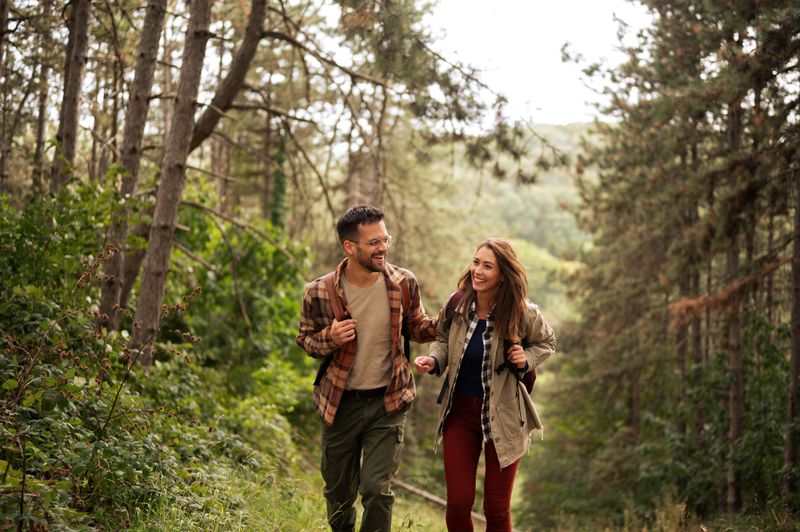 Young smiled heterosexual couple walking and exploring beautiful nature, having fun and talking, helping each other