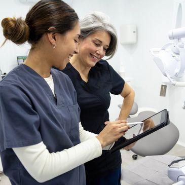 Two female dental professionals reviewing information on a digital tablet in a clinic.