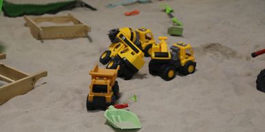 Toy construction vehicles and tools scattered in a sandbox.