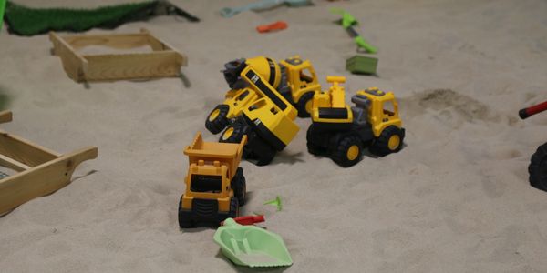Toy construction vehicles and tools scattered in a sandbox.