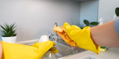 Person cleaning a kitchen sink wearing yellow gloves.