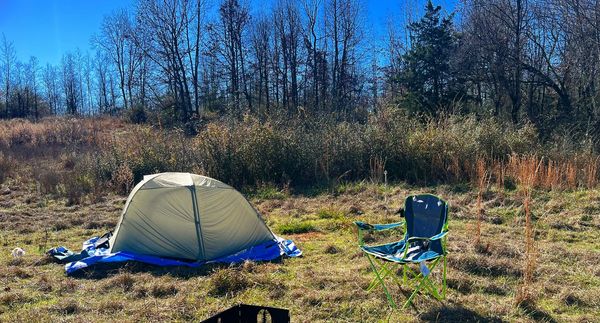 A camping setup with a tent and chair in a sunny meadow.
