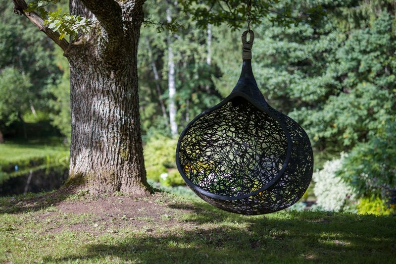 Hanging egg chair or bubble chair suspended from a tree branch. Peaceful and inviting outdoor setting for relaxation. Perfect for summer, leisure, or nature projects.