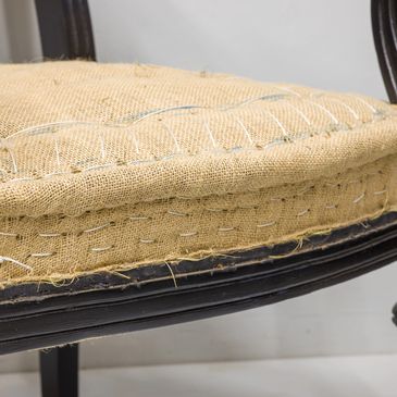 Close-up of a chair seat with burlap upholstery and dark wooden frame.