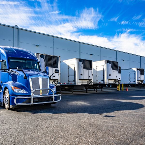 Blue semi-truck parked near loading docks with trailers.