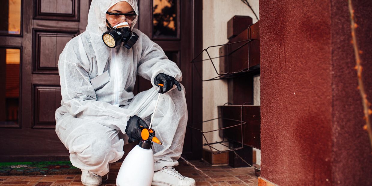 Person in protective gear spraying disinfectant outdoors.