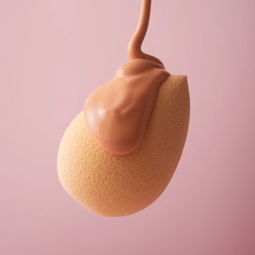Foundation being poured onto a makeup sponge against a soft pink background.